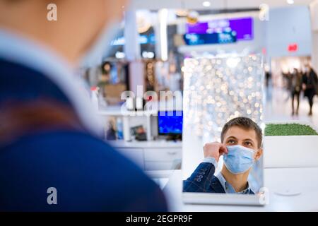 jeune homme mettant sur un masque tout en regardant dans le miroir dans le centre commercial Banque D'Images