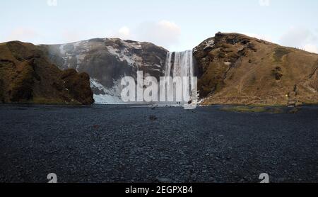 Grande cascade Skogafoss vu de loin, deux petites figures humaines au fond de la cascade Banque D'Images