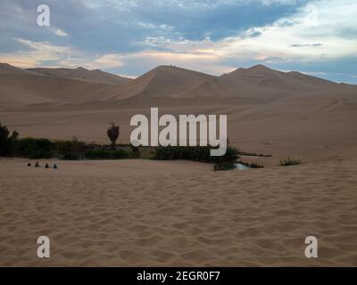 Coucher de soleil dans le désert de l'ICA, petite oasis entourée de sable, groupe de personnes assis sur le sable Banque D'Images