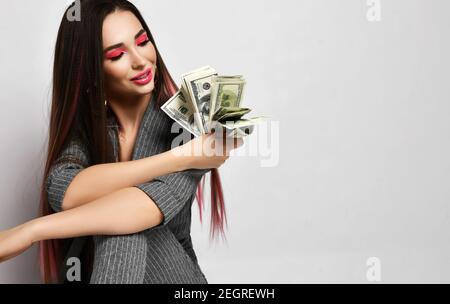 Femme d'affaires souriante et riche en pantasuit gris à fines rayures un paquet de dollars d'argent qu'elle tient en main Banque D'Images