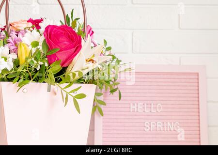 Bonjour printemps - texte sur le tableau de lettres rose feutre avec fleurs en fleur et feuilles vertes sur fond de mur de briques blanches. Concept de printemps. Habitacle desig Banque D'Images