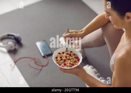 Posez la femme assise sur un tapis de fitness à la maison et en appréciant granola saine aux canneberges Banque D'Images