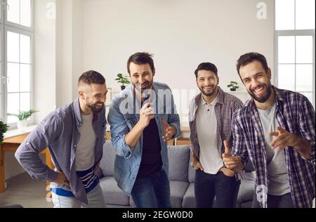 Amis masculins joyeux et positifs chantant vos chansons préférées sur un microphone karaoké ensemble pendant la fête à la maison Banque D'Images