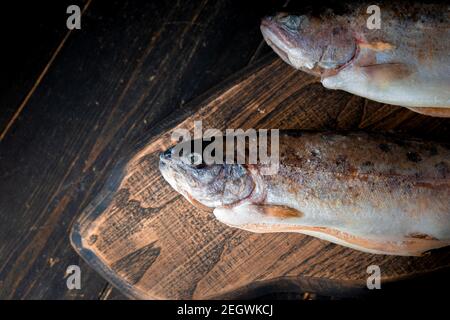 Deux truites arc-en-ciel crues avec garniture sur une planche de bois. Banque D'Images