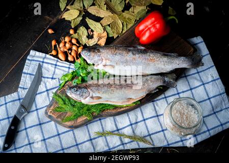 Deux truites arc-en-ciel crues avec garniture sur une planche de bois. Banque D'Images