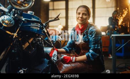 Jeune belle femme mécanicien travaille sur une moto Bobber personnalisée. Talentueuse Girl portant une chemise à carreaux et un tablier. Elle Smiles à la