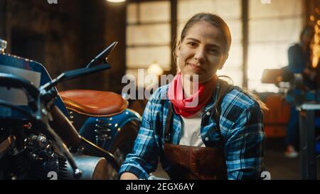 Jeune belle femme mécanicien travaille sur une moto Bobber personnalisée. Talentueuse Girl portant une chemise à carreaux et un tablier. Elle Smiles à la