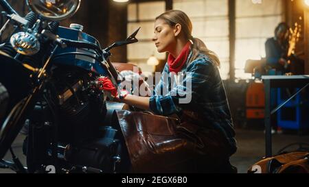 Jeune belle femme mécanicien travaille sur une moto Bobber personnalisée. Talentueuse Girl portant une chemise à carreaux et un tablier. Créatif authentique
