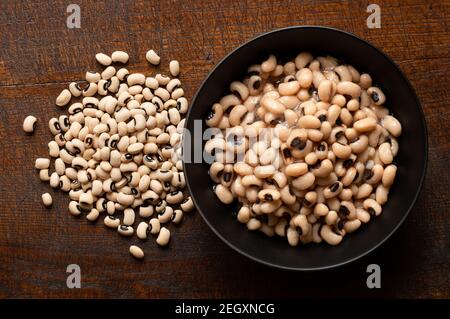 Haricots blancs cuits dans un bol en céramique noire à côté de haricots noirs non cuits isolés sur du bois. Vue de dessus. Banque D'Images