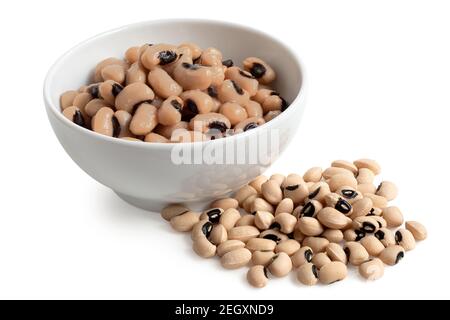 Grains cuits à yeux noirs dans un bol en céramique blanc à côté de grains non cuits à yeux noirs isolés sur du blanc. Banque D'Images