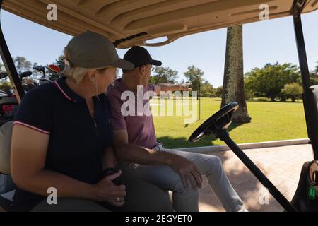 Homme et femme caucasien senior conduisant une voiturette de golf sur le golf cours parler et sourire Banque D'Images