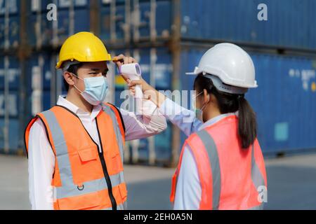 Femme asiatique contremaître balayage de la température de fièvre avec thermomètre numérique à Son travailleur portant un masque d'hygiène protège contre le coronavirus Ou COVI Banque D'Images