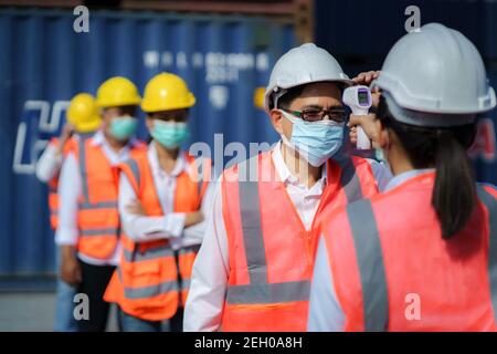 Femme asiatique contremaître balayage de la température de fièvre avec thermomètre numérique à Son travailleur portant un masque d'hygiène protège contre le coronavirus Ou COVI Banque D'Images