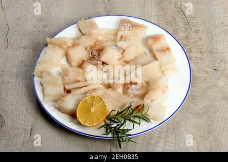 Filet de poisson de mer piqué sur une assiette blanche décorée de citron et de romarin, poisson blanc brut sur une assiette, fond en bois gris Banque D'Images