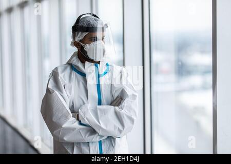 Un médecin de sexe masculin en costume de protection et un masque médical se trouve près d'une fenêtre dans un hôpital. Banque D'Images