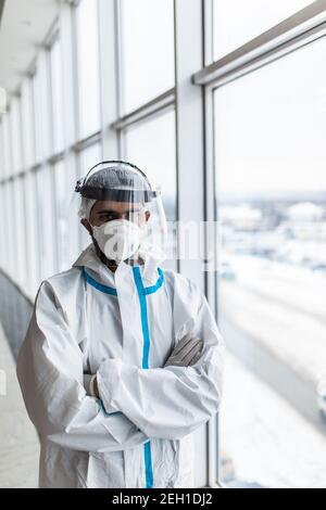 Un médecin de sexe masculin en costume de protection et un masque médical se trouve près d'une fenêtre dans un hôpital. Banque D'Images