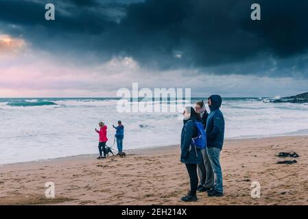 Une famille de vacanciers se tenant sur une plage de Fistral venteuse et profitant de la vue sur la baie de Fistral à Newquay, dans les Cornouailles. Banque D'Images