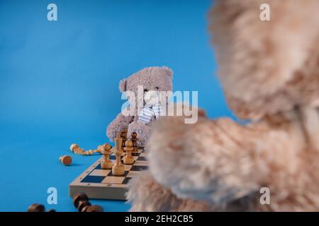 Gros plan sur les ours en peluche avec des pièces d'échecs sur l'échiquier. Jouets en peluche qui jouent aux échecs sur fond bleu Banque D'Images