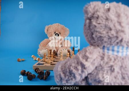 Gros plan sur les ours en peluche avec des pièces d'échecs sur l'échiquier. Jouets en peluche qui jouent aux échecs sur fond bleu Banque D'Images