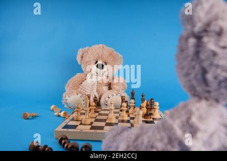 Gros plan sur les ours en peluche avec des pièces d'échecs sur l'échiquier. Jouets en peluche qui jouent aux échecs sur fond bleu Banque D'Images