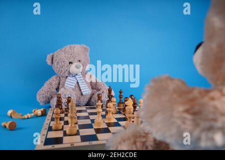 Gros plan sur les ours en peluche avec des pièces d'échecs sur l'échiquier. Jouets en peluche qui jouent aux échecs sur fond bleu Banque D'Images