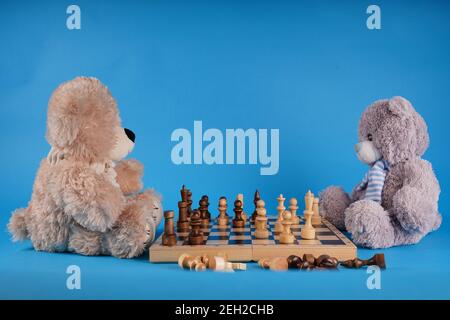 Gros plan sur les ours en peluche avec des pièces d'échecs sur l'échiquier. Jouets en peluche qui jouent aux échecs sur fond bleu Banque D'Images