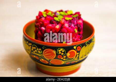 Salade de betteraves russes Vinegret de légumes bouillis dans un bol en bois peint sur fond de table blanc. Banque D'Images