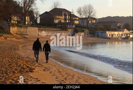 Couple hétérosexuel marchant sur la plage Playa de los Bikinis un matin ensoleillé sur le bord de la baie de Santander Cantabria Espagne Banque D'Images