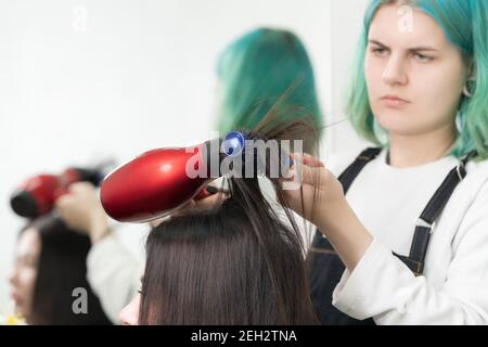 Lady coiffstylist séchage des cheveux brunette avec sèche-cheveux rouge et brosse à cheveux bleue dans le salon de beauté Banque D'Images