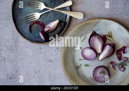 Oignon rouge dans des assiettes bleues et grises, avec des feuilles de romarin et deux fourchettes. Banque D'Images