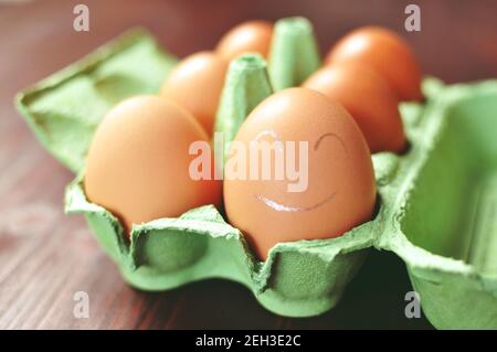 Groupe d'oeufs de poulet brun dans une forme ouverte verte travail sur fond brun. L'œuf le plus proche est peint avec un visage smiley blanc. Vue avant. Banque D'Images