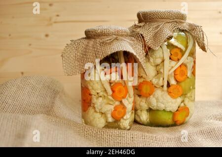 Concept de deux cornichons saisonniers pot avec des tomates crues, de couleur verte, orange et Carotte Chou-fleur blanc sur fond de bois naturel. Banque D'Images