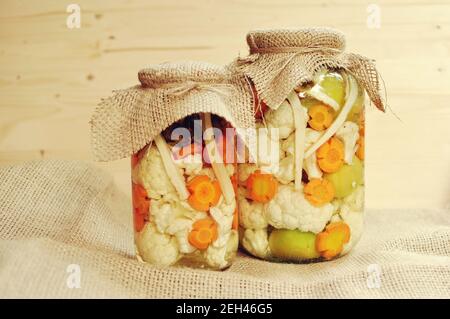 Concept de deux cornichons saisonniers pot avec des tomates crues, de couleur verte, orange et Carotte Chou-fleur blanc sur fond de bois naturel. Banque D'Images