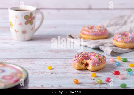 Piquer de délicieux beignets aux fraises avec du glaçage rose, des saupoudres colorées et des haricots en gelée sur fond de bois. Pâtisserie sucrée comme encas pour les enfants Banque D'Images