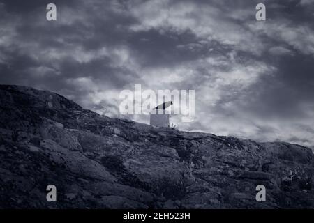 La colline du parc national de Peneda Geres avec un corbeau sur un site géodésique contre un ciel nuageux. Bleu noir et blanc. Banque D'Images