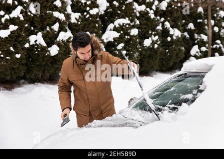 Un homme nettoie la neige et la glace des essuie-glaces de sa voiture. Banque D'Images