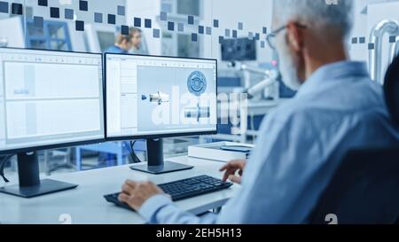 Au-dessus de l'épaule : ingénieur principal de l'industrie lourde travaillant sur un ordinateur personnel, l'écran montre le logiciel de CAO avec le prototype 3D de moteur électrique Banque D'Images