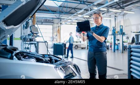 Femme Mechanic utilise une tablette avec un logiciel de diagnostic de réalité augmentée. Un spécialiste inspecte la voiture pour la trouver cassée Banque D'Images