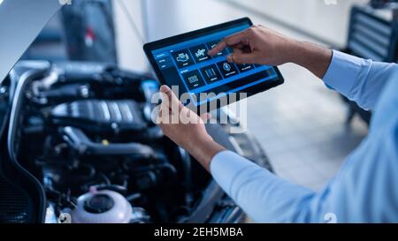 Car Service Manager ou Mechanic utilise une tablette avec un logiciel de diagnostic interactif futuriste. Un spécialiste inspecte le véhicule dans l'ordre Banque D'Images