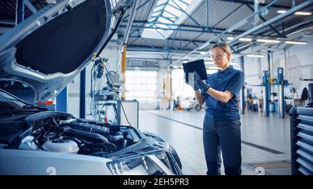 Femme Mechanic utilise une tablette avec un logiciel de diagnostic de réalité augmentée. Un spécialiste inspecte la voiture pour la trouver cassée Banque D'Images