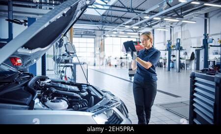 Femme Mechanic utilise une tablette avec un logiciel de diagnostic de réalité augmentée. Un spécialiste inspecte la voiture pour la trouver cassée Banque D'Images