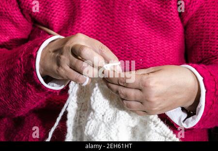 Gros plan d'une femme en chandail rouge triant du fil de laine blanc avec les aiguilles à la main Banque D'Images
