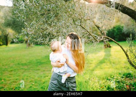 Femme tenant sa petite fille dans ses bras sous un olivier un jour ensoleillé Banque D'Images