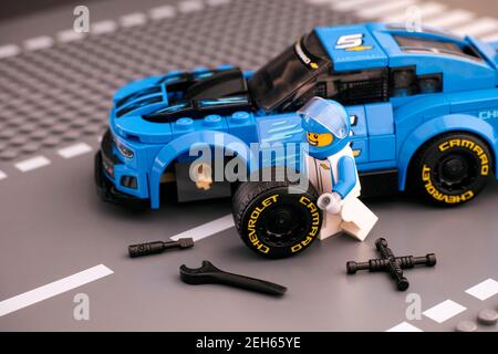 Tambov, Fédération de Russie - le 14 février 2021 le pilote de Lego minifigure fixe la roue de la voiture de course ZL1 de Chevrolet Camaro par LEGO Speed Champions. Base de la route Banque D'Images