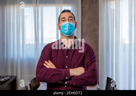 Homme barbu dans une chemise violette avec un masque pour se protéger du coronavirus avec ses bras croisés. Concept d'attente Banque D'Images
