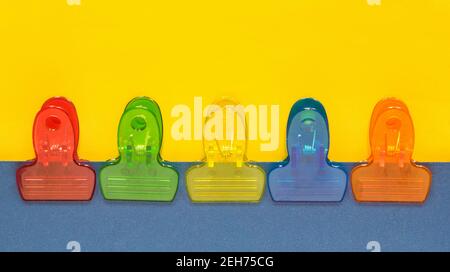 Pinces de reliure en plastique coloré rangées avec un arrière-plan de séparation bleu et jaune et un espace de copie. Banque D'Images