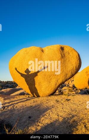 Bloc en forme de coeur avec ombre de l'homme avec les bras étirés. Dans la lumière du soir dorée au parc national de Joshua Tree, CA carte de Saint-Valentin approprié. Banque D'Images