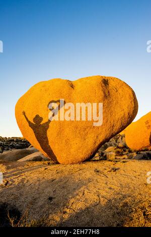 Bloc en forme de coeur avec ombre d'un homme tenant une couronne de coeur. Dans la lumière du soir dorée au parc national de Joshua Tree, CA carte de Saint-Valentin approprié. Banque D'Images