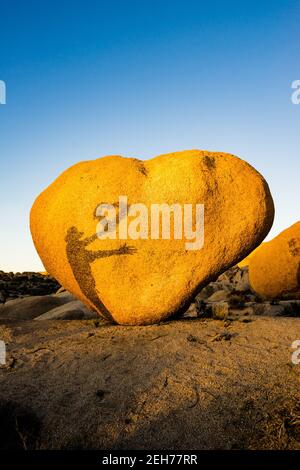 Bloc en forme de coeur avec ombre d'un homme tenant une couronne de coeur. Dans la lumière du soir dorée au parc national de Joshua Tree, CA carte de Saint-Valentin approprié. Banque D'Images