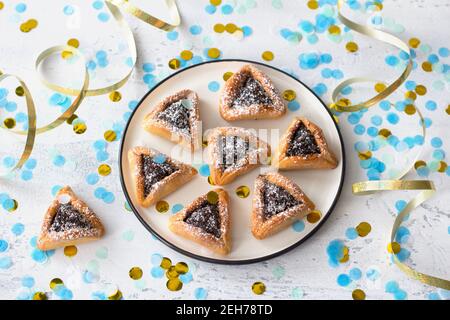 Biscuits faits maison au hamantashen (oreilles de Haman) aux graines de pavot et aux pommes dans une atmosphère festive avec des confettis sur fond gris clair. Concept de c Banque D'Images